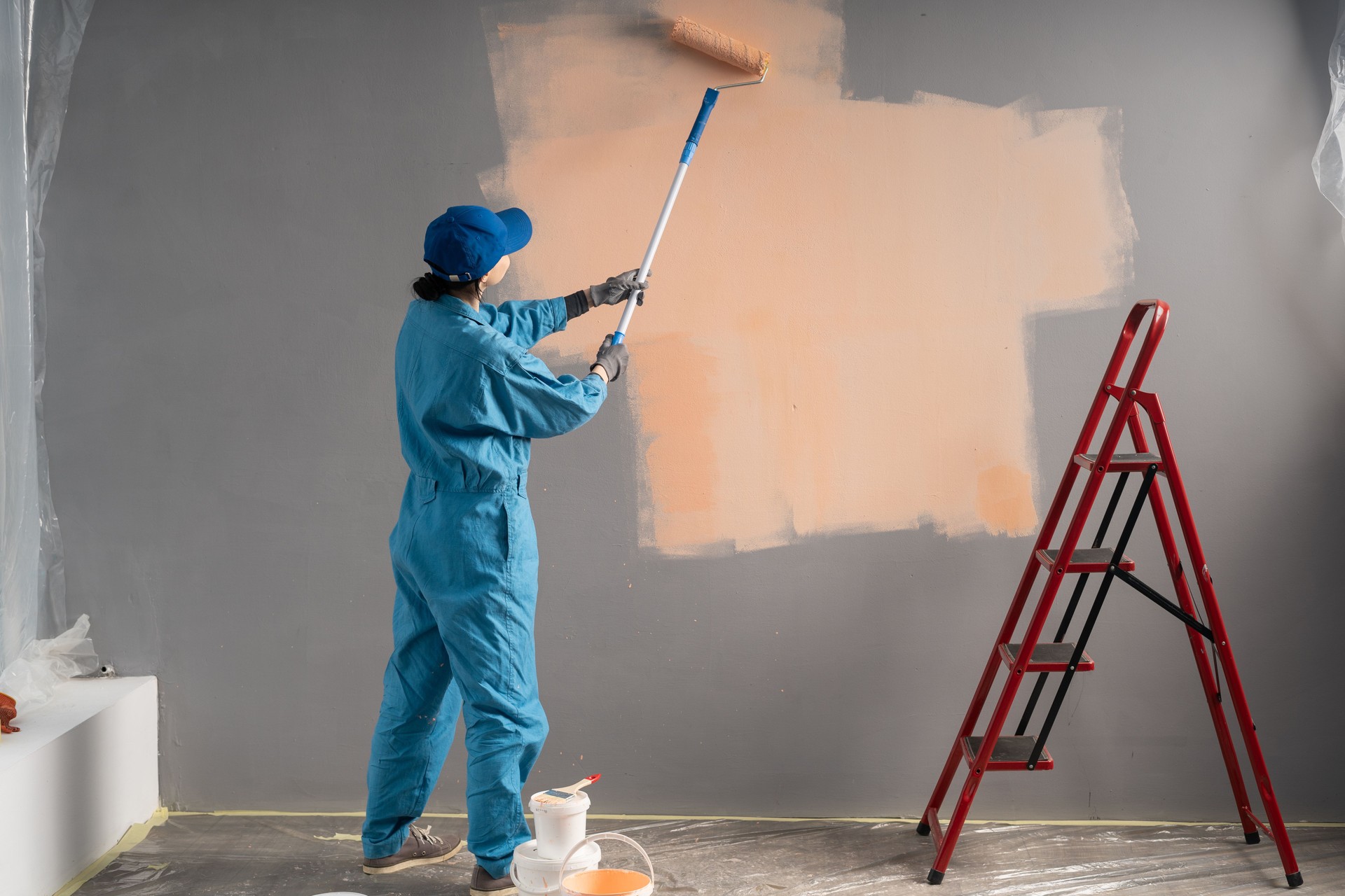 Builder or painter in cap Paints walls with long painting roller. business, building, renovation and people