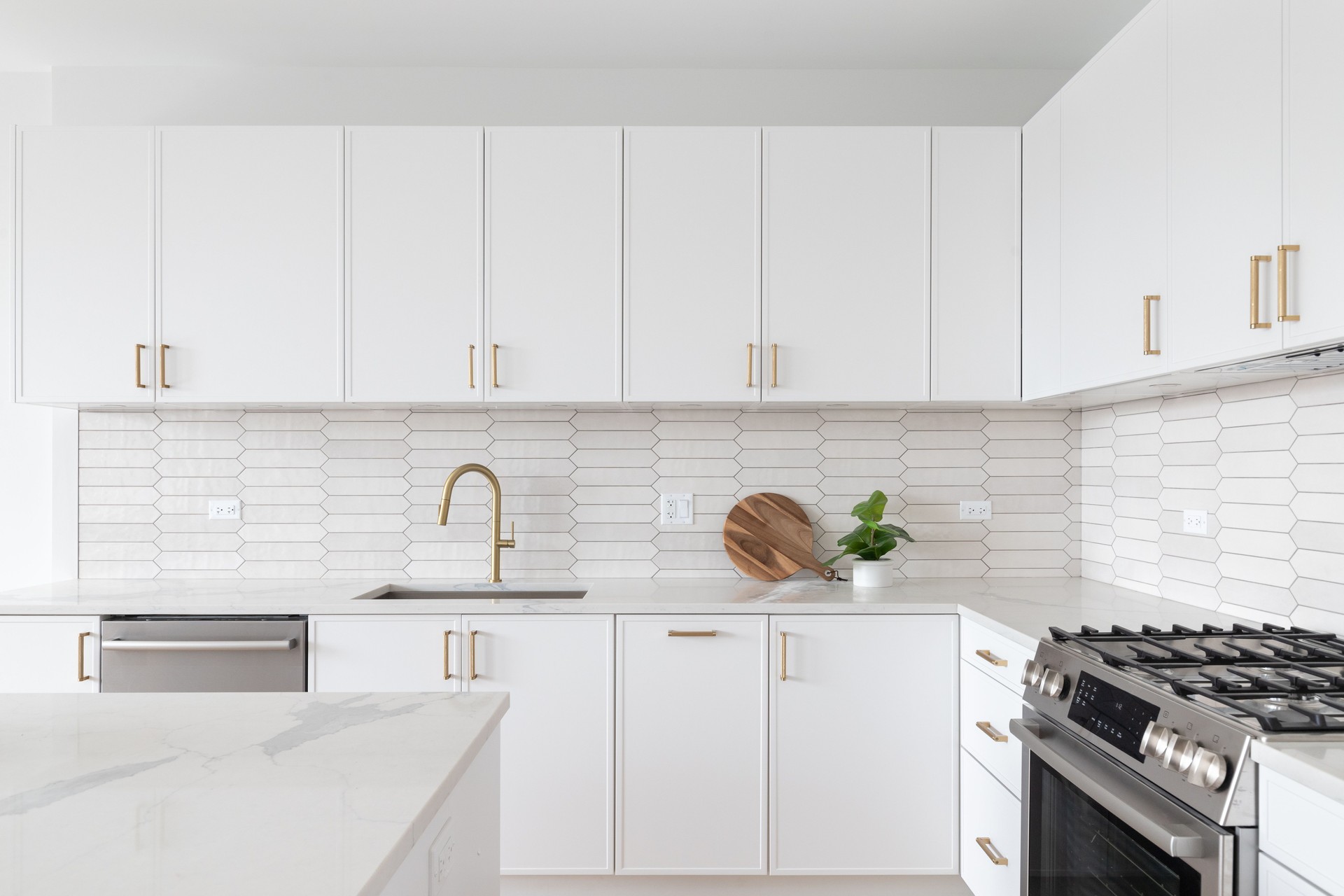 A white kitchen with gold faucet and hardware and a brown picket tile backsplash.